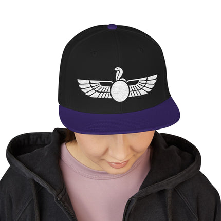 Black snapback hat featuring white embroidered Egyptian Uraeus winged cobra symbol.