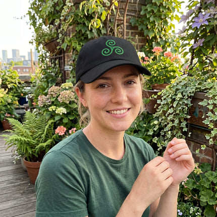 Black baseball cap with green embroidered Celtic Triskelion symbol.