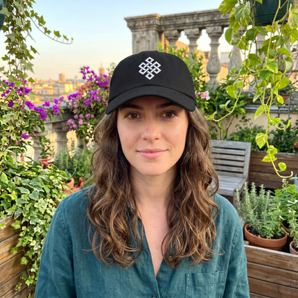 Black baseball cap embroidered with the white Endless Knot symbol, representing Buddhist interconnectedness.