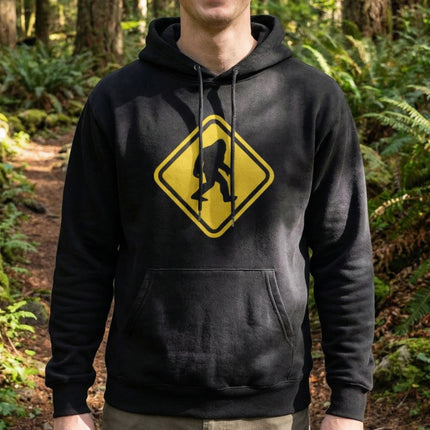 Black hoodie featuring a yellow warning sign with a Bigfoot crossing silhouette graphic.
