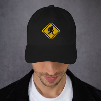 Embroidered Bigfoot crossing sign cap featuring a sasquatch warning symbol graphic.