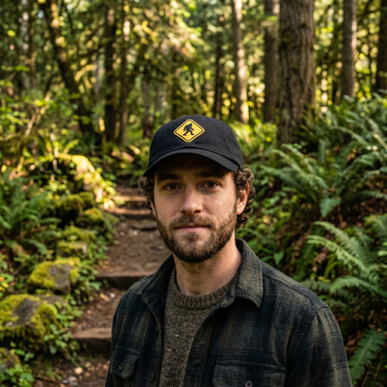 Black baseball cap featuring an embroidered Bigfoot crossing warning sign.